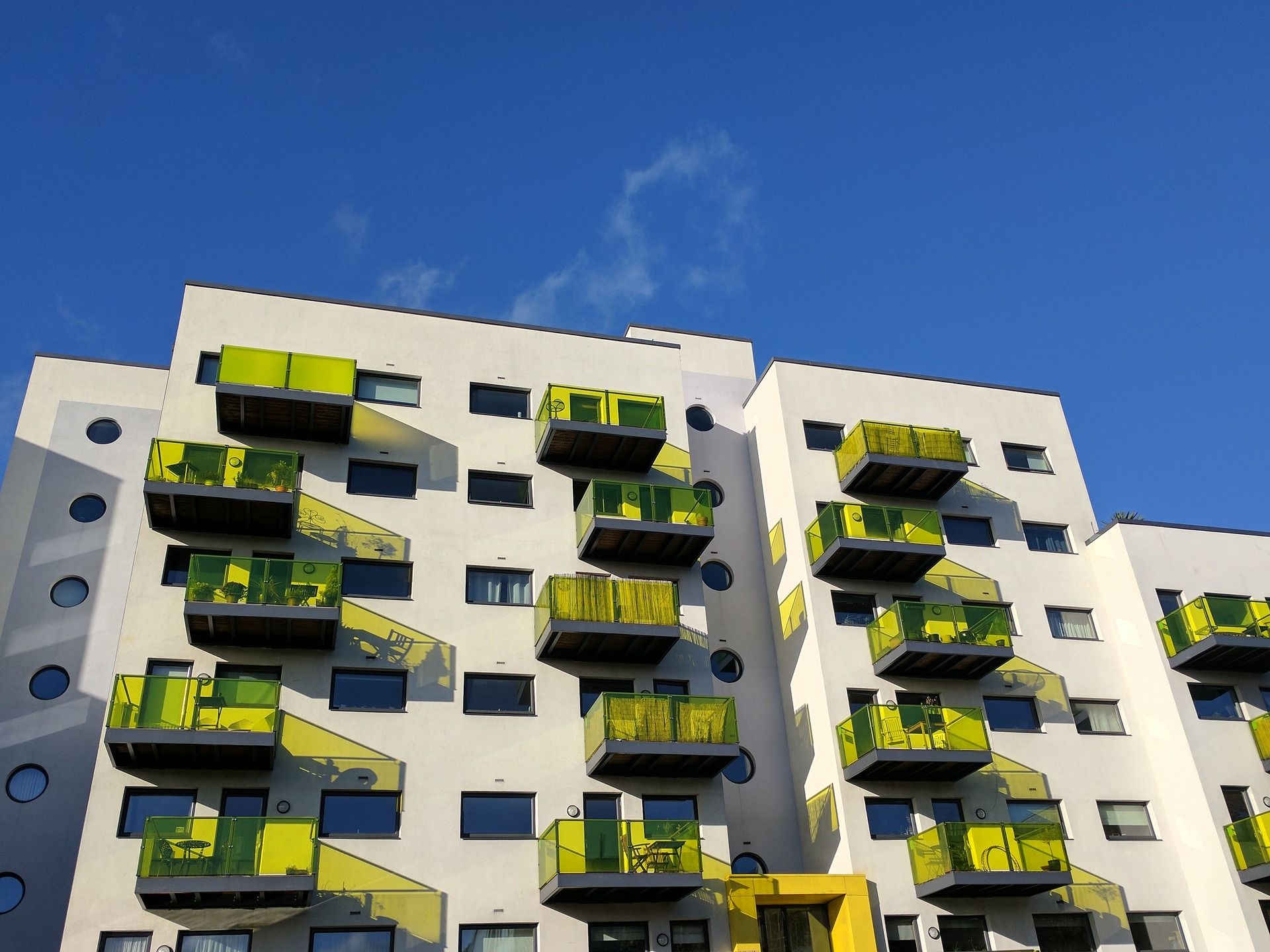 Block of flats in England with green glass balconies set against a blue sky